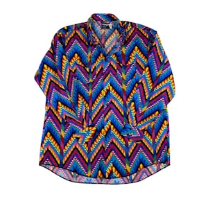 May include: A long-sleeved button-down shirt with a vibrant, geometric pattern. The shirt features a repeating chevron design in shades of blue, yellow, pink, and black. The collar and cuffs are visible, and the shirt is laid flat against a white background.