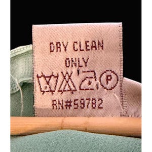May include: Close-up of a clothing care label with the words "DRY CLEAN ONLY" in red. The label also features care symbols and the number "RN#59782". The label is attached to a light green garment.