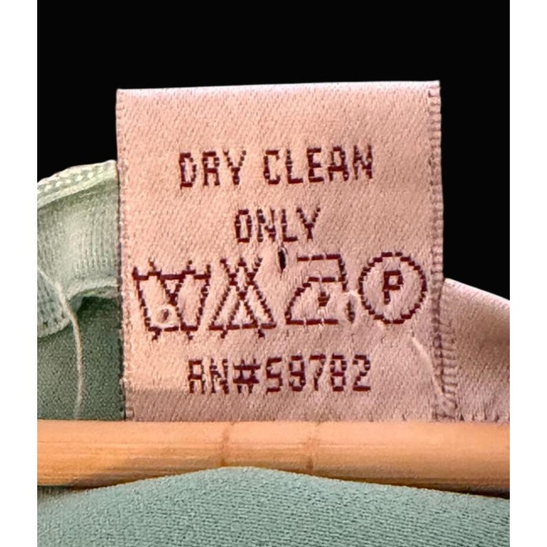 May include: Close-up of a clothing care label with the words "DRY CLEAN ONLY" in red. The label also features care symbols and the number "RN#59782". The label is attached to a light green garment.