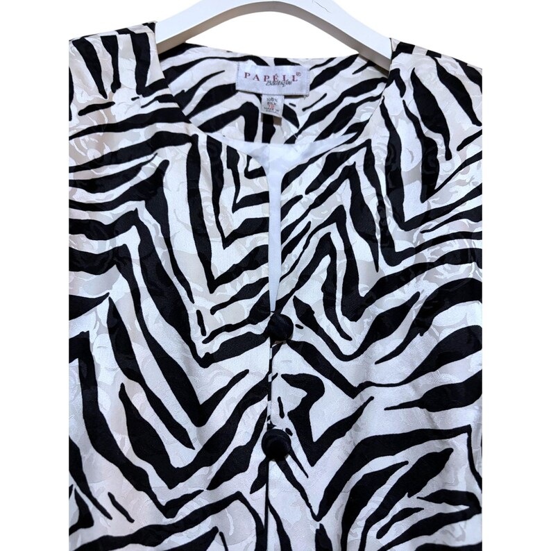 Puede incluir: Chaqueta con estampado de cebra en blanco y negro con tres botones negros en la parte delantera. La chaqueta est&aacute; colgada de una percha blanca. El nombre de la marca "Pabell" es visible en la etiqueta.