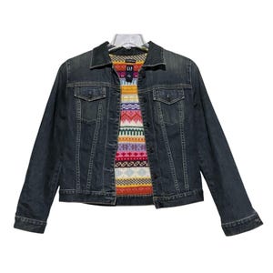 May include: A dark wash denim jacket with a colorful patterned lining. The jacket has a classic collar, button-up front, and two chest pockets. The lining features a geometric design in various colors, including red, yellow, and blue.