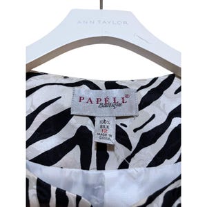 Puede incluir: Primer plano de una chaqueta de seda Papell Boutique con estampado de cebra en blanco y negro. La etiqueta indica que la chaqueta es talla 12 y est&aacute; hecha de 100% seda.