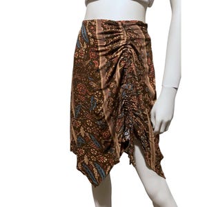 May include: A brown skirt with a floral pattern in shades of pink, blue, and beige. The skirt has a ruched detail on the side and a unique asymmetrical hemline. The fabric appears to be lightweight and flowing, suitable for warm weather.