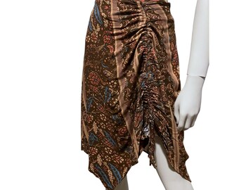May include: A brown skirt with a floral pattern in shades of pink, blue, and beige. The skirt has a ruched detail on the side and a unique asymmetrical hemline. The fabric appears to be lightweight and flowing, suitable for warm weather.