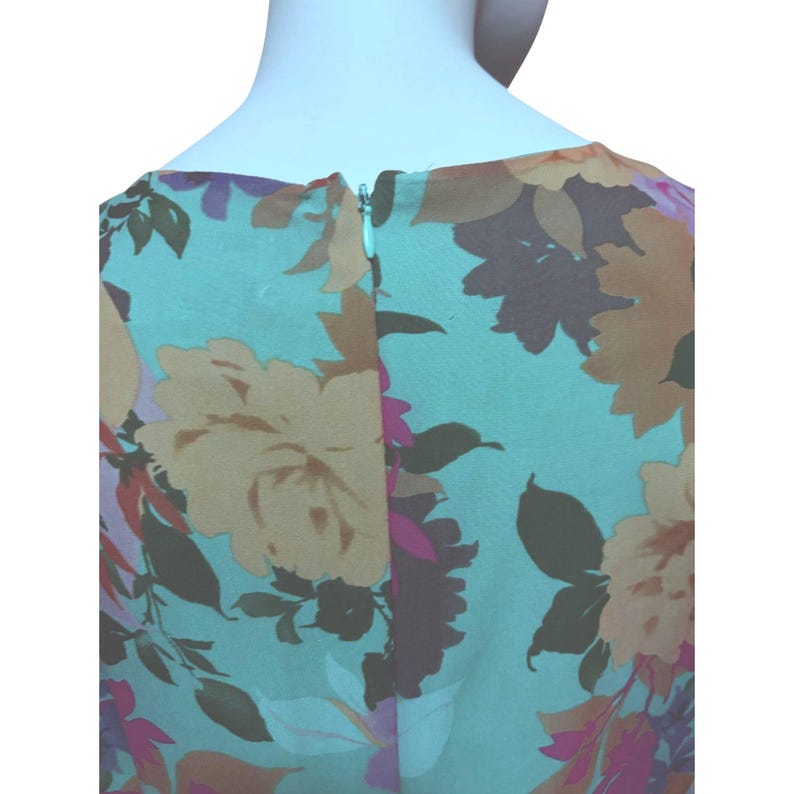 May include: A sleeveless dress with a floral pattern. The dress features a light blue background with large flowers in shades of yellow, brown, and pink. A zipper runs down the back of the dress.