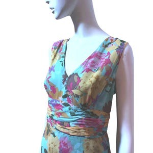 May include: A sleeveless floral dress with a V-neck. The dress features a light blue background with a pattern of pink, yellow, and brown flowers. The waist is cinched with a gathered fabric detail.