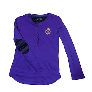 May include: A long-sleeved purple shirt with a Henley neckline and button closure. The shirt features a gold emblem with the letters "RL" and a crown. The elbow patches have a patterned design. The shirt is made of a soft material.