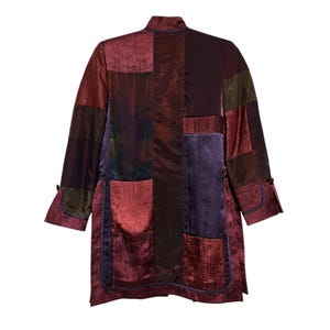 May include: A patchwork coat in shades of burgundy, purple, and olive green. The coat features a mandarin collar, long sleeves, and a knee-length design. The fabric has a textured, iridescent finish, with a dark blue trim.