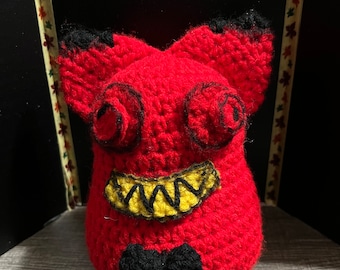 May include: A red crocheted plush toy with black eyes, a yellow and black mouth, and a black bow tie.
