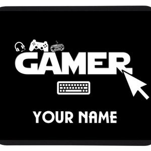 以下が含まれることがあります： 黒と白の マウスパッド に、大きな白い文字で「GAMER」と書かれており、キーボードのアイコン、ジョイスティックのアイコン、ヘッドセットのアイコン、マウスカーソルが描かれています。「YOUR NAME」という文字が「GAMER」の下にあります。