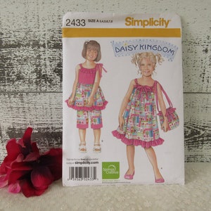 May include: Simplicity sewing pattern number 2433, Daisy Kingdom, for girls' dresses and shorts. The pattern includes a pink and white floral print dress with a ruffled hem, a matching bag, and a pair of pink and white floral print shorts.