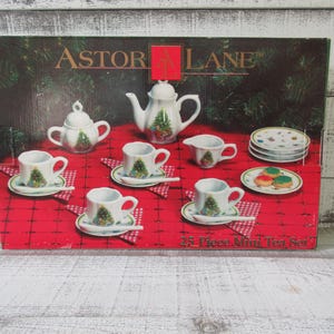 Peut inclure: Un service à thé miniature de 25 pièces Astor Lane dans une boîte sur fond de nappe rouge. Le service en céramique blanche comprend une théière, un sucrier, un pot à lait, des tasses, des soucoupes et des assiettes à motif sapin de Noël.