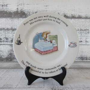 May include: White ceramic plate featuring a rabbit in bed illustration, with text around the rim. The plate includes a teapot and teacup illustration. Text reads: "Peter was not very well during the evening. His mother put him to bed. and made some camomile tea: One teaspoonful to be taken at bedtime."