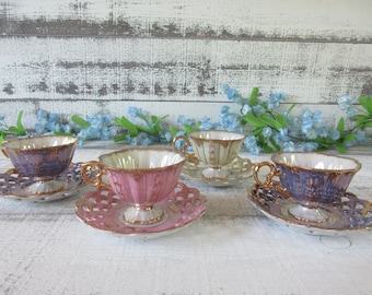 Puede incluir: Tres tazas de té de porcelana con platillos que presentan un diseño acanalado con bordes y asas dorados. Una taza es rosa, mientras que las otras dos son de color púrpura iridiscente. Cada platillo tiene un borde decorativo con calado.
