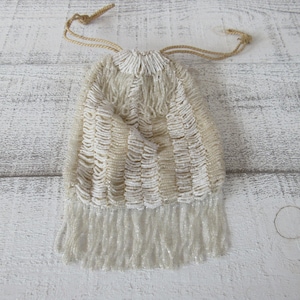 Op de afbeelding: Een witte kralen tas met trekkoord en een franje rand. De tas is gemaakt van kleine, witte kralen en heeft een eenvoudig, elegant ontwerp.