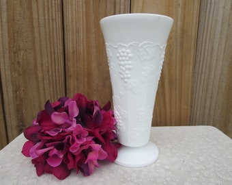 May include: White milk glass vase with a grapevine design. The vase has a flared top and a pedestal base.