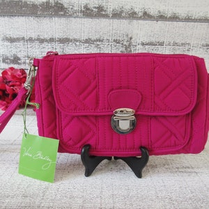 May include: A pink quilted clutch with a silver clasp and a detachable wrist strap. The clutch has a Vera Bradley tag attached to it.