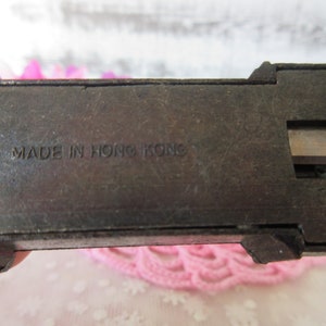 Puede incluir: Un sacapuntas vintage de metal con acabado negro. El sacapuntas tiene un solo agujero y una cuchilla de metal. El sacapuntas tiene el texto "MADE IN HONG KONG" impreso en la parte inferior.