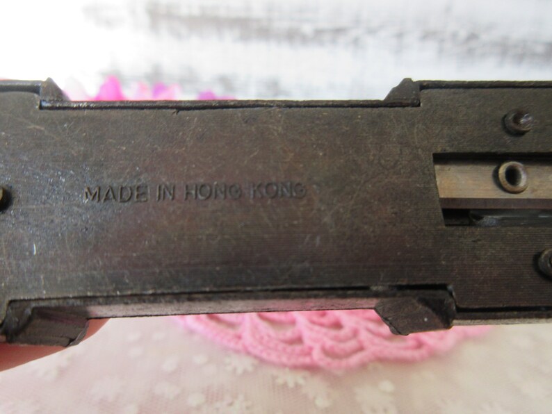 Puede incluir: Un sacapuntas vintage de metal con acabado negro. El sacapuntas tiene un solo agujero y una cuchilla de metal. El sacapuntas tiene el texto "MADE IN HONG KONG" impreso en la parte inferior.