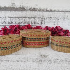May include: Three oval-shaped woven baskets with red and green trim. The baskets are made of natural materials and have a rustic look.