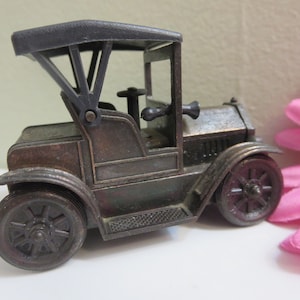 Puede incluir: Un sacapuntas de metal de estilo vintage con forma de coche con un techo de plástico negro. El coche es marrón y tiene un diseño detallado.