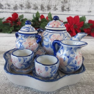 May include: A blue and white porcelain tea set with pink floral designs. The set includes a teapot, creamer, sugar bowl, two cups and saucers, and a tray.