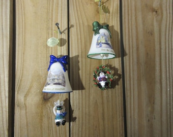 May include: Four Christmas ornaments hanging on a wooden surface. Two bell-shaped ornaments with blue and green bows, and a snowman ornament. The bells have detailed images and text. The snowman ornament is in a wreath.