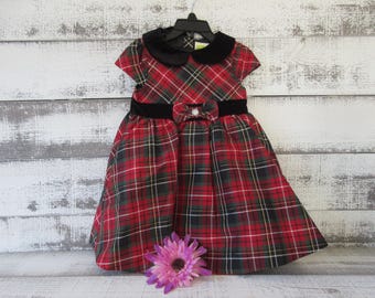Könnte beinhalten: Ein rot-grün-weiß kariertes Kleid mit schwarzem Samtkragen und Taillengürtel. Das Kleid hat eine Schleife mit Perlendetail an der Taille und kurze Ärmel. Eine lila Blume befindet sich am unteren Rand des Kleides.