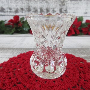 Può includere: Un vaso di fiori in vetro trasparente con un design in vetro tagliato. Il vaso ha un bordo smerlato e una base rotonda.