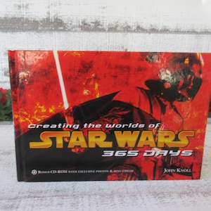 May include: A hardback book titled "Creating the Worlds of Star Wars 365 Days" with a red and black cover featuring Darth Vader and a lightsaber. The book includes a bonus CD-ROM with exclusive photos and mini-videos.
