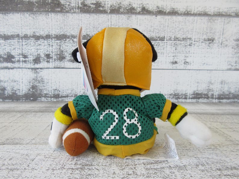 May include: A plush toy in a football uniform, viewed from the back. The toy has a yellow helmet with a tan stripe, a green jersey with the number 28, and a brown football. The arms have black and yellow stripes.