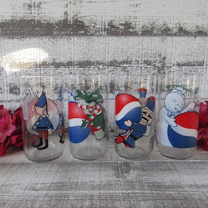 May include: Set of four vintage glass tumblers featuring a Christmas theme. Each tumbler has a different character, including a snowman, an elf, a Santa Claus, and a gingerbread man. The tumblers are clear glass with colorful illustrations.