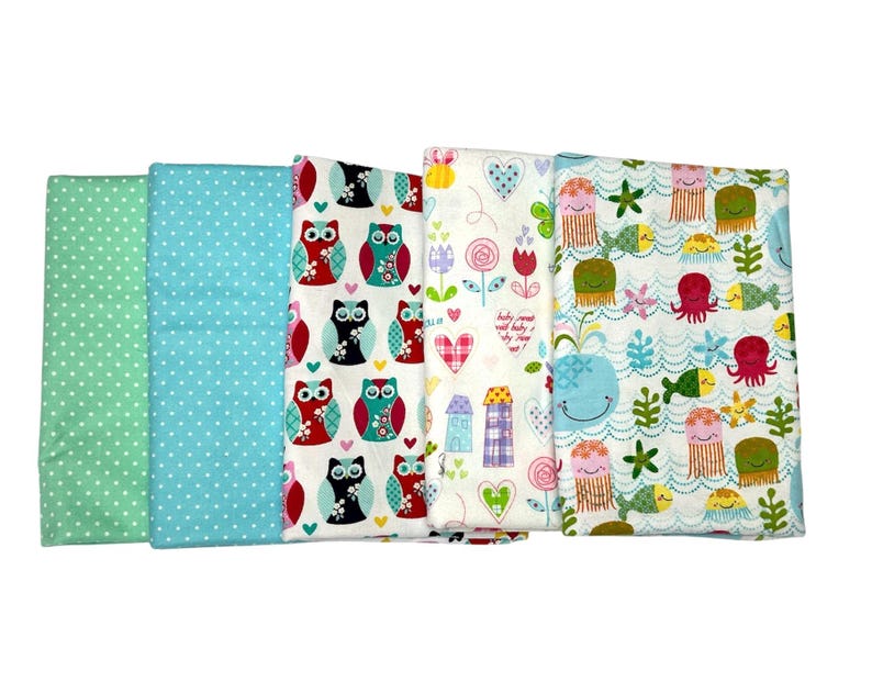 May include: Four fabric squares with different patterns. One square has a green background with white polka dots. Another square has a light blue background with white polka dots. A third square has a white background with colorful owls. The last square has a white background with colorful sea creatures and the text "Baby comes with baby, dry them up".