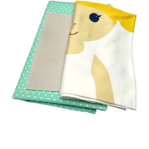 May include: A set of three fabric squares for crafting. The top square features a cartoon girl with blonde hair and a blue eye. The middle square is a solid beige color. The bottom square is a light green fabric with white polka dots.