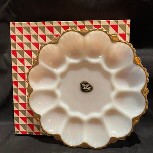May include: A white milk glass egg plate with a gold rim and a "Milk White" label. The plate has 12 individual indentations for holding eggs.