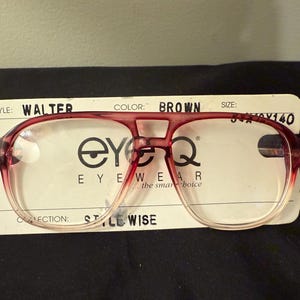 May include: Red and clear plastic eyeglasses with a brown frame. The eyeglasses are labeled "Walter" and "Style Wise" on the tag. The tag also includes the brand name "EyeQ Eyewear".