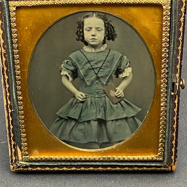 Ambrotype antique 1/6 th plate tinted photograph of a young girl holding what looks like a book.