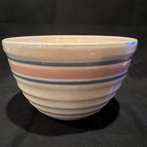 May include: A white ceramic mixing bowl with blue and pink stripes. The bowl has a wavy, textured exterior.