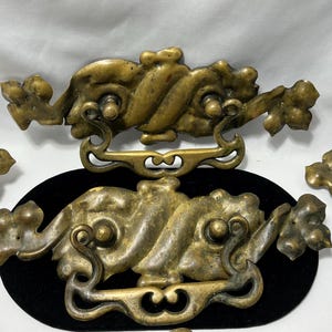 May include: Antique brass drawer pulls with ornate, cloud-like designs. The hardware features intricate details and a warm, aged patina. These vintage pulls are ideal for adding a touch of classic elegance to furniture.