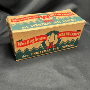May include: A vintage cardboard box for Westinghouse Mazda Christmas tree lights. The box is green and brown with a red and white illustration of a Christmas tree light bulb. The text on the box reads "Westinghouse Mazda Lamps for Christmas Tree Lighting."