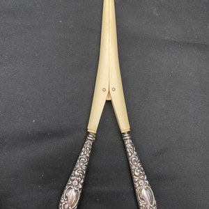 May include: A pair of antique silver and ivory nutcrackers. The handles are ornately decorated with floral designs. The nutcracker is closed and ready to crack nuts.