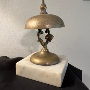 Op de afbeelding: Een messingbel met een decoratief handvat en een marmeren voet. De bel wordt gebruikt als een servicebel.