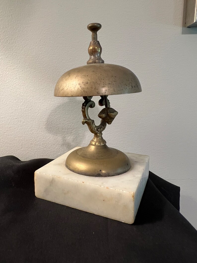 Op de afbeelding: Een messingbel met een decoratief handvat en een marmeren voet. De bel wordt gebruikt als een servicebel.