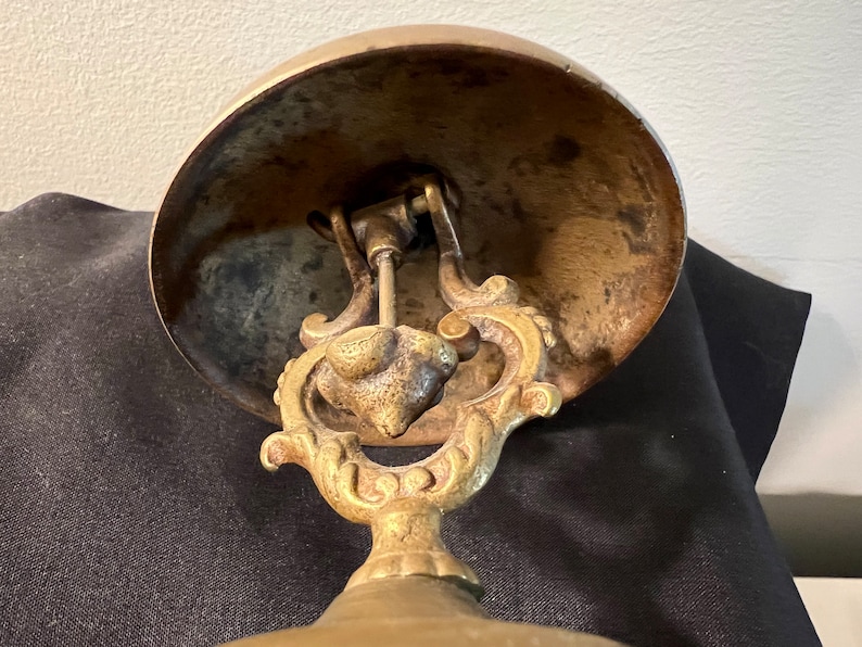 Op de afbeelding: Antiek messing bel met een decoratief handvat en een ronde basis. De bel heeft een versleten, verweerde afwerking.