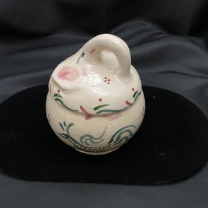 May include: A white ceramic jar with a lid and a handle. The jar is decorated with green, pink, and black floral designs.