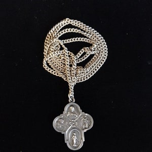 May include: A silver chain necklace with a silver pendant featuring a four-sided cross with religious imagery.