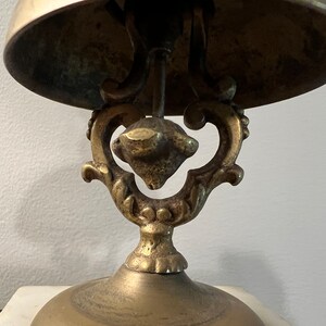 Op de afbeelding: Een messing bel met een sierlijke basis. De bel is gemonteerd op een decoratieve standaard met een gerold ontwerp.
