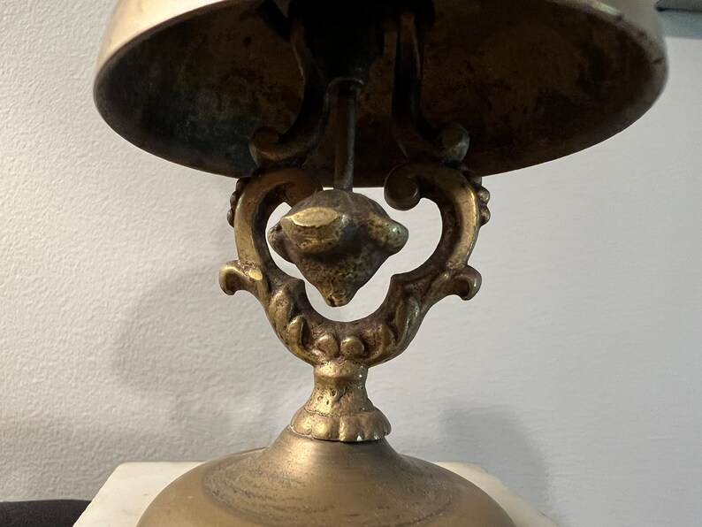 Op de afbeelding: Een messing bel met een sierlijke basis. De bel is gemonteerd op een decoratieve standaard met een gerold ontwerp.