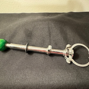 May include: A silver sugar tong with a green marble handle. The tong has a spring-loaded mechanism and is designed to grip sugar cubes.