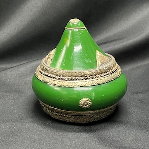 May include: A small, green, ceramic trinket box with a conical lid and silver-colored metal trim. The box has a decorative floral design around the rim.